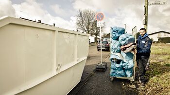 Container zur Entrümpelung mit Mitarbeiter und Müll auf Wagen